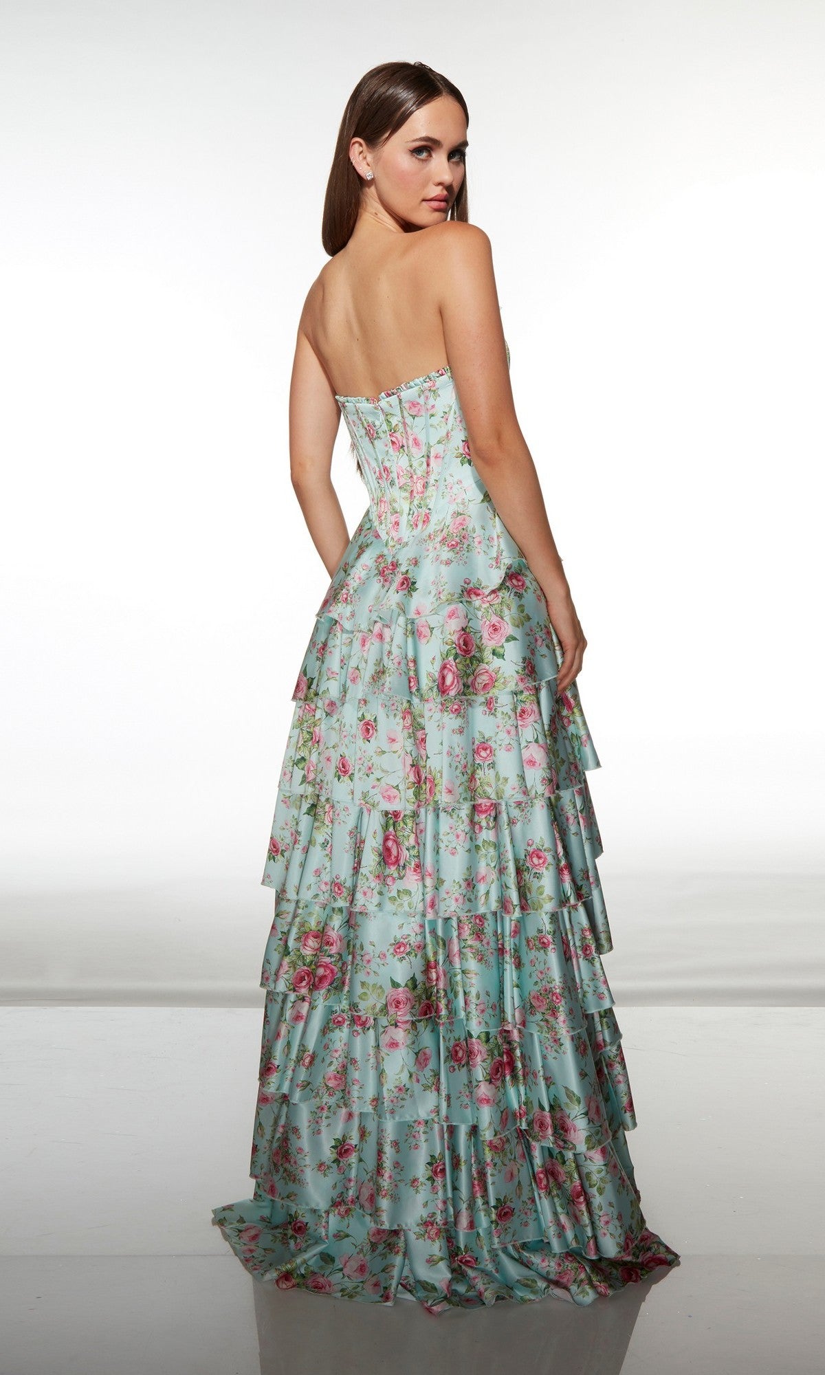 A woman stands with her back to the camera against a plain background, modeling the Alyce 62066, a long strapless floral prom dress featuring a corset bodice and tiered ruffle skirt.
